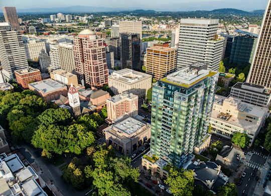 A cityscape with a mix of modern and older buildings, surrounded by greenery.