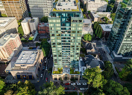 A tall green building stands in the middle of a city intersection.