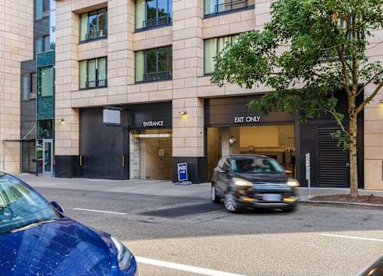 A blue car is parked on the side of the road in front of a building with an entrance.