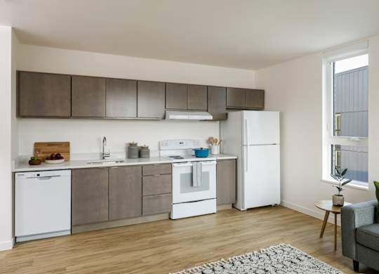 A modern kitchen with white appliances and a grey couch.