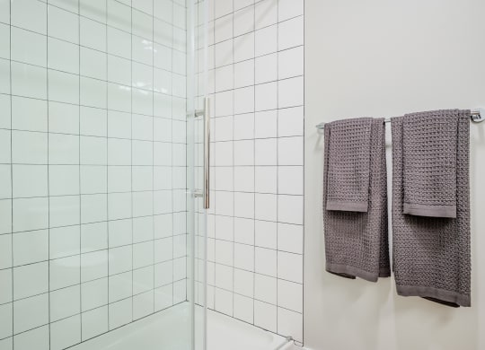 a white tiled bathroom with two towels hanging on the wall at Slabtown Square Apartments, Portland 