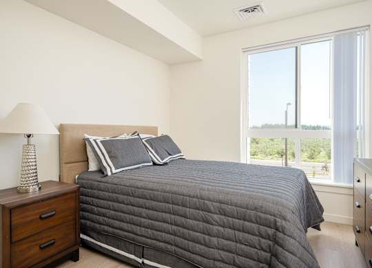 A bedroom with a large bed and a lamp on a nightstand.
