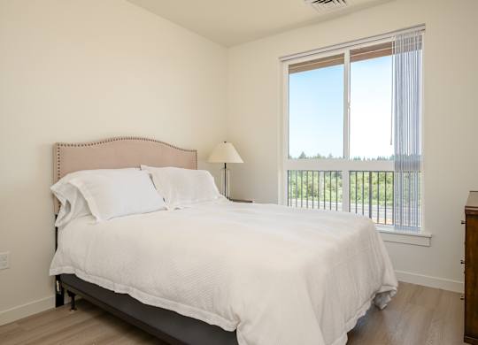 A bedroom with a large bed and a window overlooking a balcony.