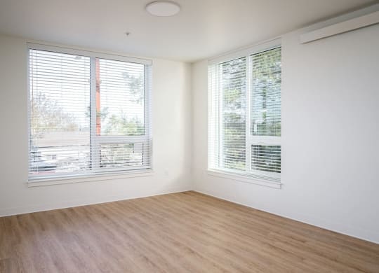 an empty room with two windows and wood floors