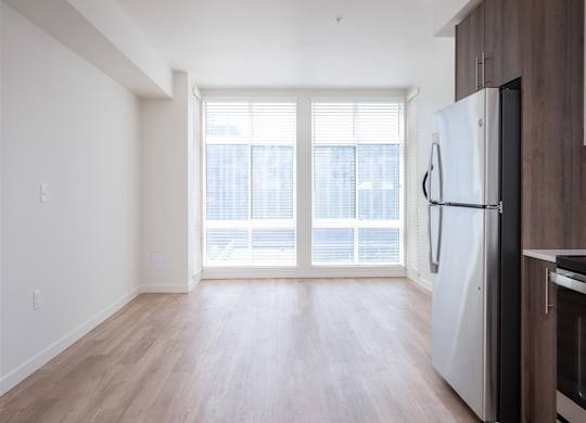 an empty living room with a large window and a refrigerator