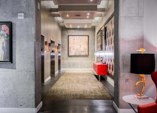 a hallway with a rug and paintings on the wall and a red chair and table