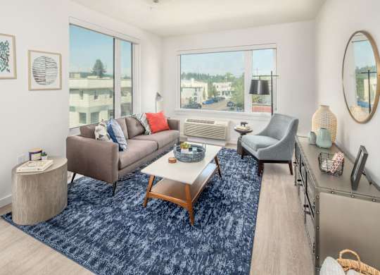 A living room with a grey couch, a brown armchair, a blue rug, and a wooden coffee table.