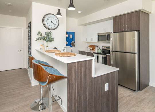 A modern kitchen with a bar stool and a clock on the wall.