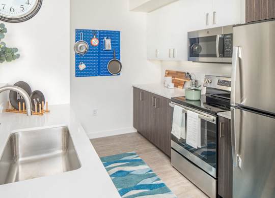 A modern kitchen with a stainless steel refrigerator, a sink, and a clock on the wall.