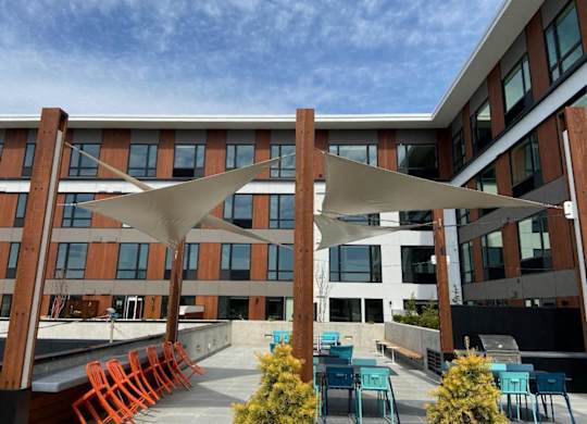 A modern building with orange chairs and tables under a white canopy.