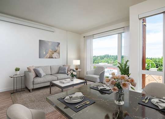 A modern living room with a grey sofa, a glass table, and a large window.
