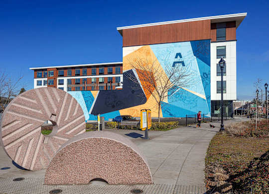 A building with a mural on the side has a bench in front of it.