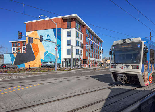 A train is on the tracks in front of a building with a colorful mural.