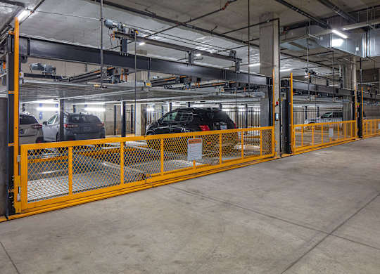 A parking garage with a yellow railing and a black car in the background.