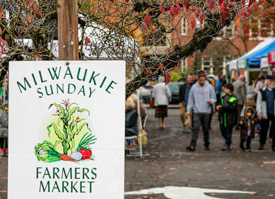 A sign for the Milwaukie Sunday Farmers Market is displayed on a pole.