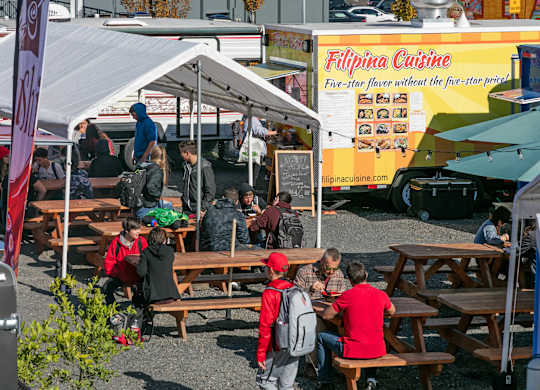 A food truck with the name Filipina Cuisine on it is parked at a food court.