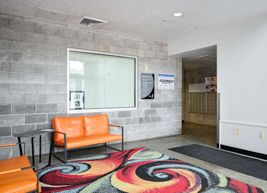 a lobby with orange chairs and a colorful rug and a window