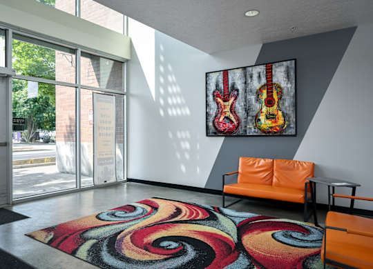 a living room with a colorful rug and a guitar painting on the wall