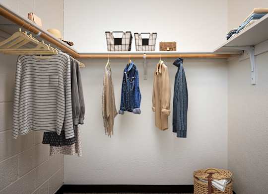 a closet with clothes hanging on the wall and a wooden shelf on the ceiling