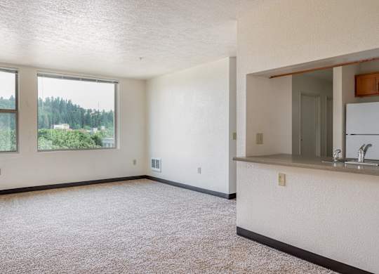 an empty living room with a kitchen and a large window