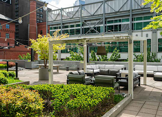 A patio with a white pergola and grey couches.