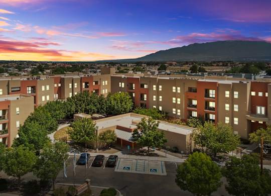 A sunset view of a large apartment complex with a parking lot in front.