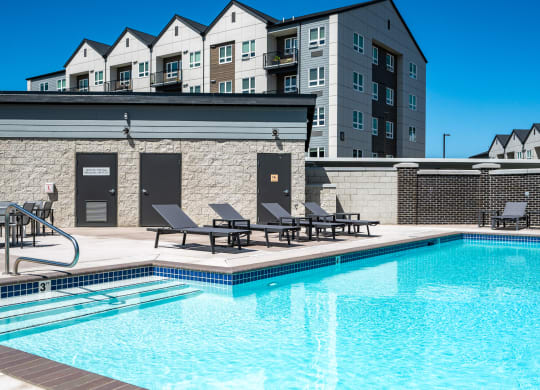 a swimming pool with chairs and a building in the background