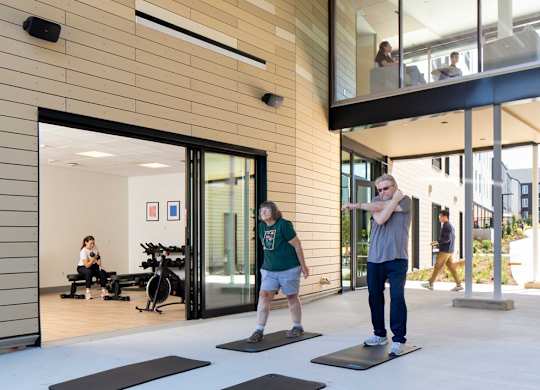 A man and a woman are exercising in a gym with wooden walls and ceiling.