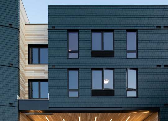 A modern building with a black facade and a wooden entrance.