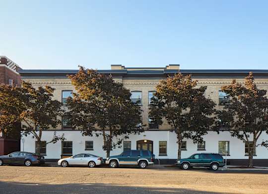 A white building with a black roof and a green car parked in front.