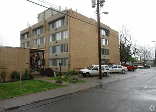A grey building with a parking lot in front.