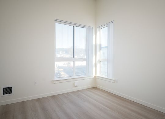 A room with two windows and a wooden floor.