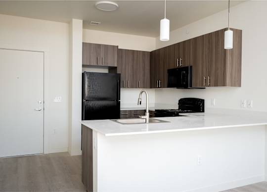 A kitchen with a black fridge and microwave, brown cabinets, and a white countertop.