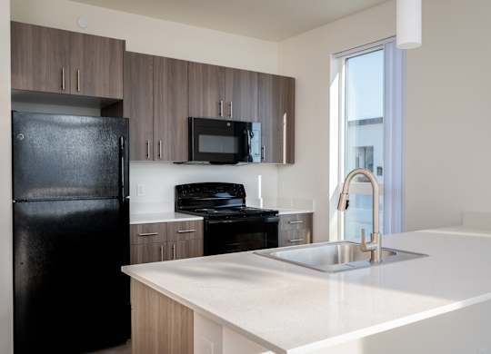A black fridge stands next to a white counter in a modern kitchen.