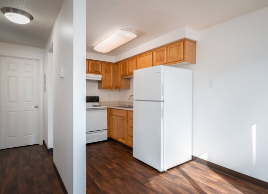 an empty kitchen with a white refrigerator and wooden cabinets