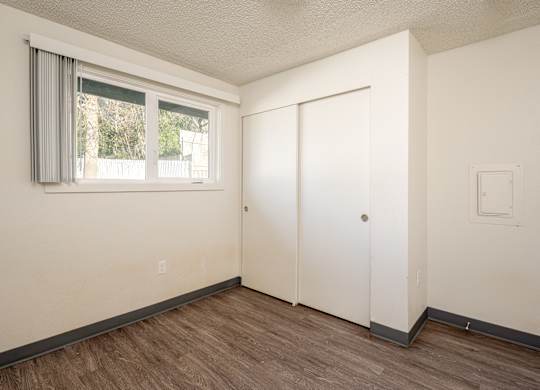 A room with a white door, a window with grey curtains, and a light switch on the wall.