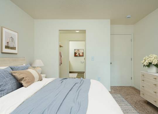 A bedroom with a large bed and a dresser with a vase of flowers on top.