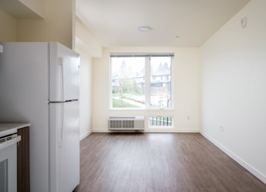 an empty living room with a refrigerator and a window