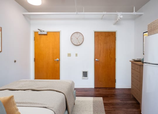 a bedroom with a bed and a refrigerator and a clock on the wall