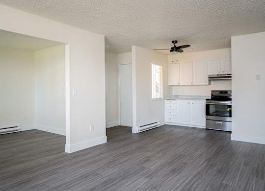A room with a ceiling fan and a kitchen area in the background.