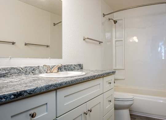 A bathroom with a marble countertop and white fixtures.