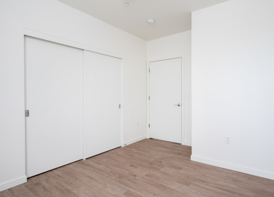 a bedroom with white walls and wood flooring and two closets