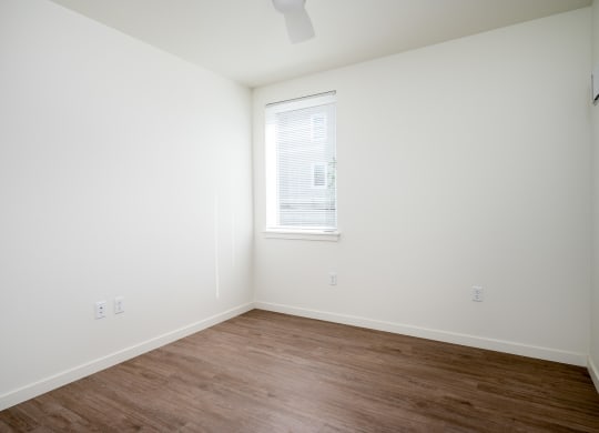a bedroom with white walls and a window and wood floors