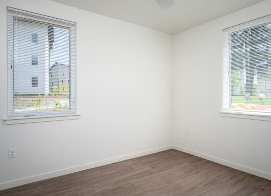 an empty room with two windows and a wooden floor