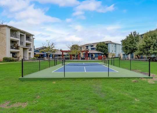 A tennis court is surrounded by apartment buildings.