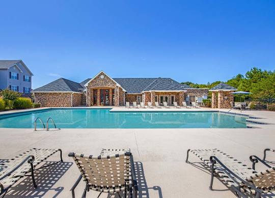 A pool with a stone building in the background at Ethan Pointe Apartments, Greensboro, NC, 27215