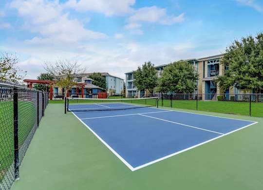 A tennis court is surrounded by a black fence and a building is in the background.