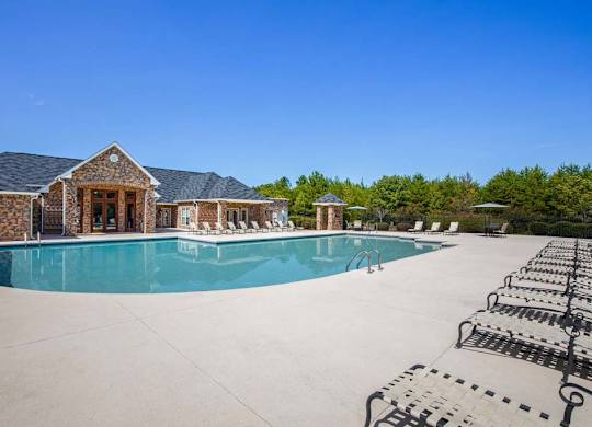 A large swimming pool is surrounded by a concrete patio and a house with a stone wall at Ethan Pointe Apartments, Greensboro, 27215