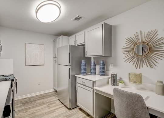 A kitchen with a refrigerator, microwave, and a desk with a chair.