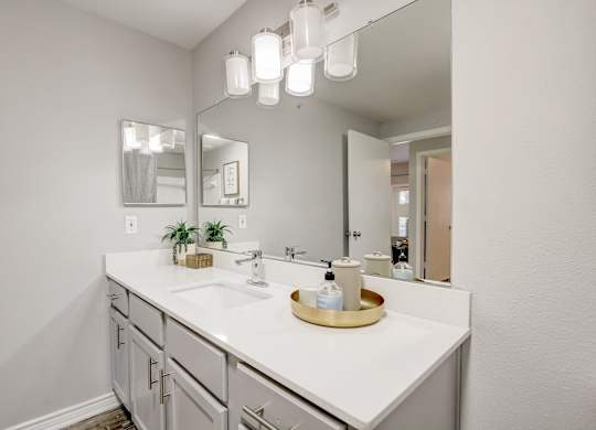 A bathroom with a white counter top and a mirror above it.